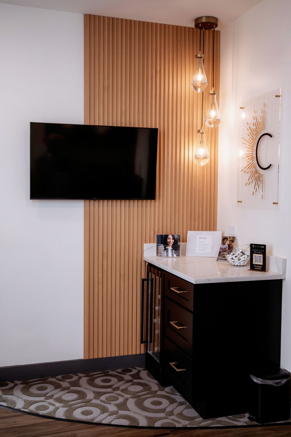 Contemporary dental office waiting area featuring wood accent wall, mounted TV, and pendant lighting.