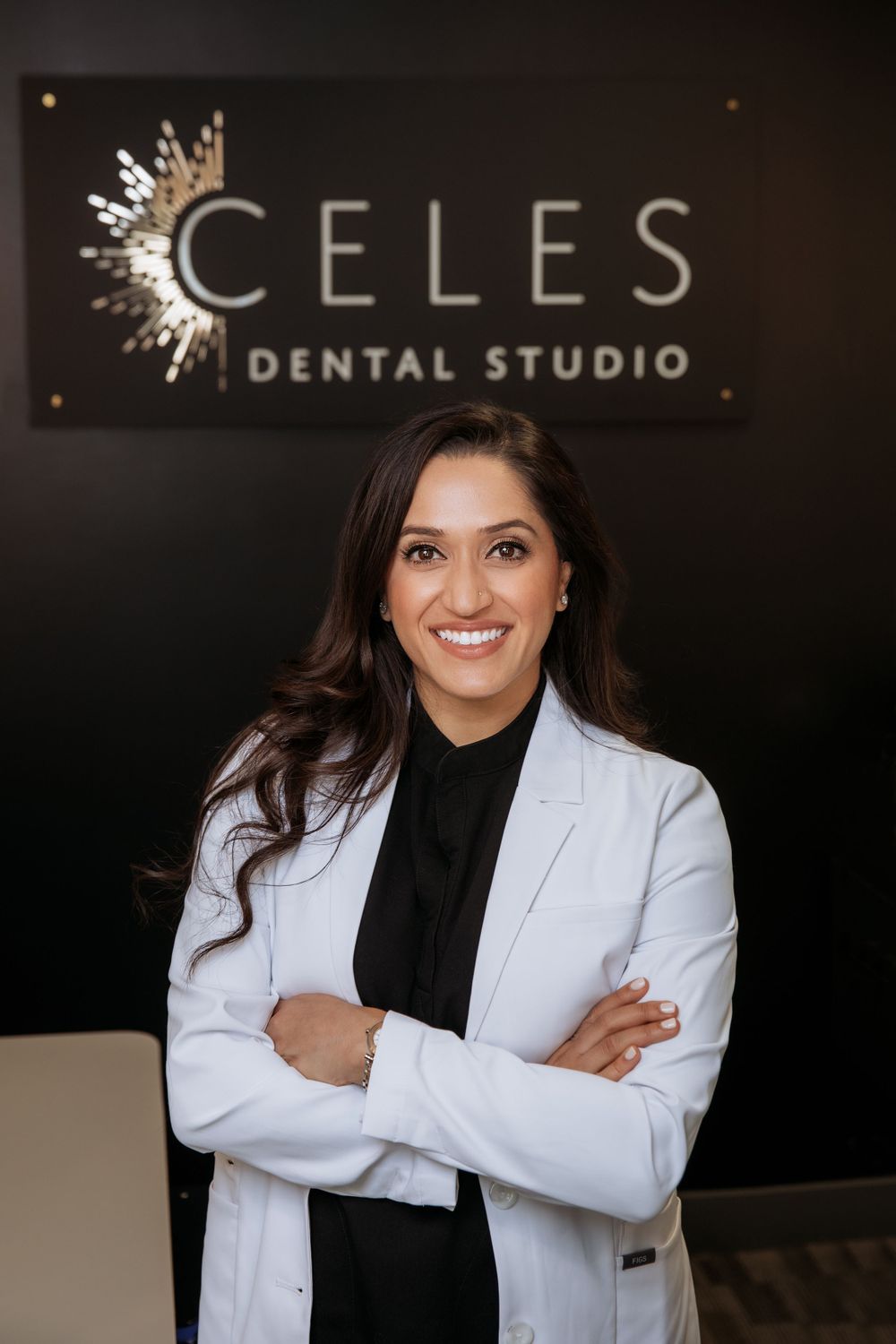 Dental professional in white coat standing confidently in front of Celes Dental Studio signage.