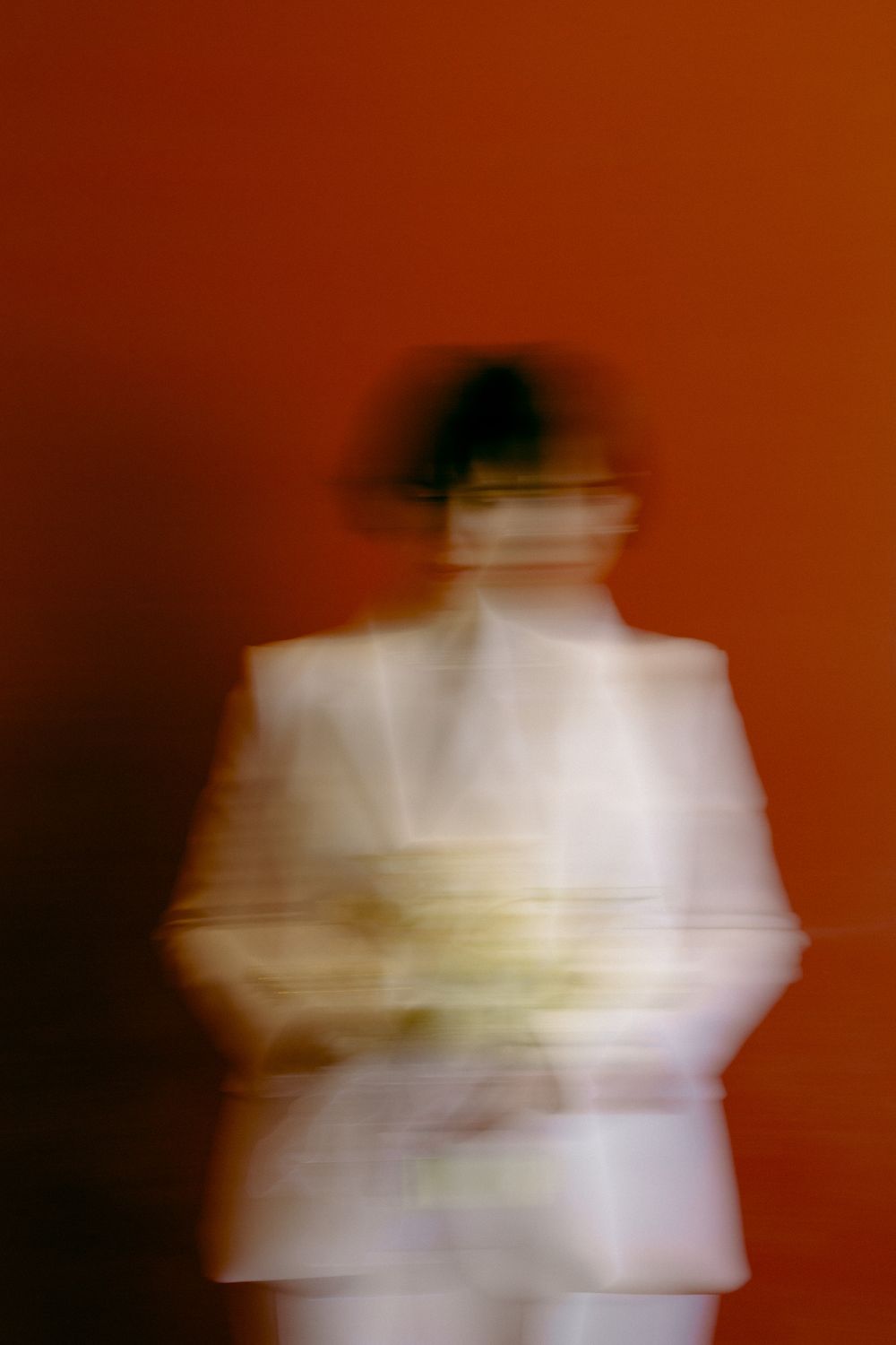 An artistic motion blur portrait of a person in white against a deep red background.