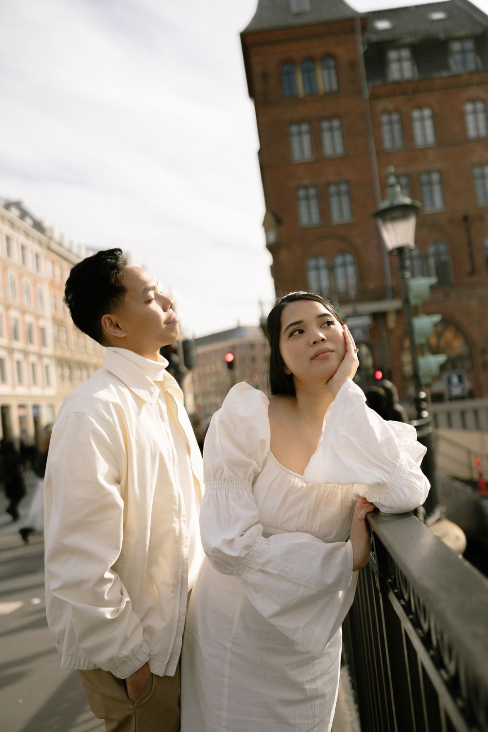 A couple in white clothing poses on a bridge with historic architecture in the background. Copenhagen, Denmark.