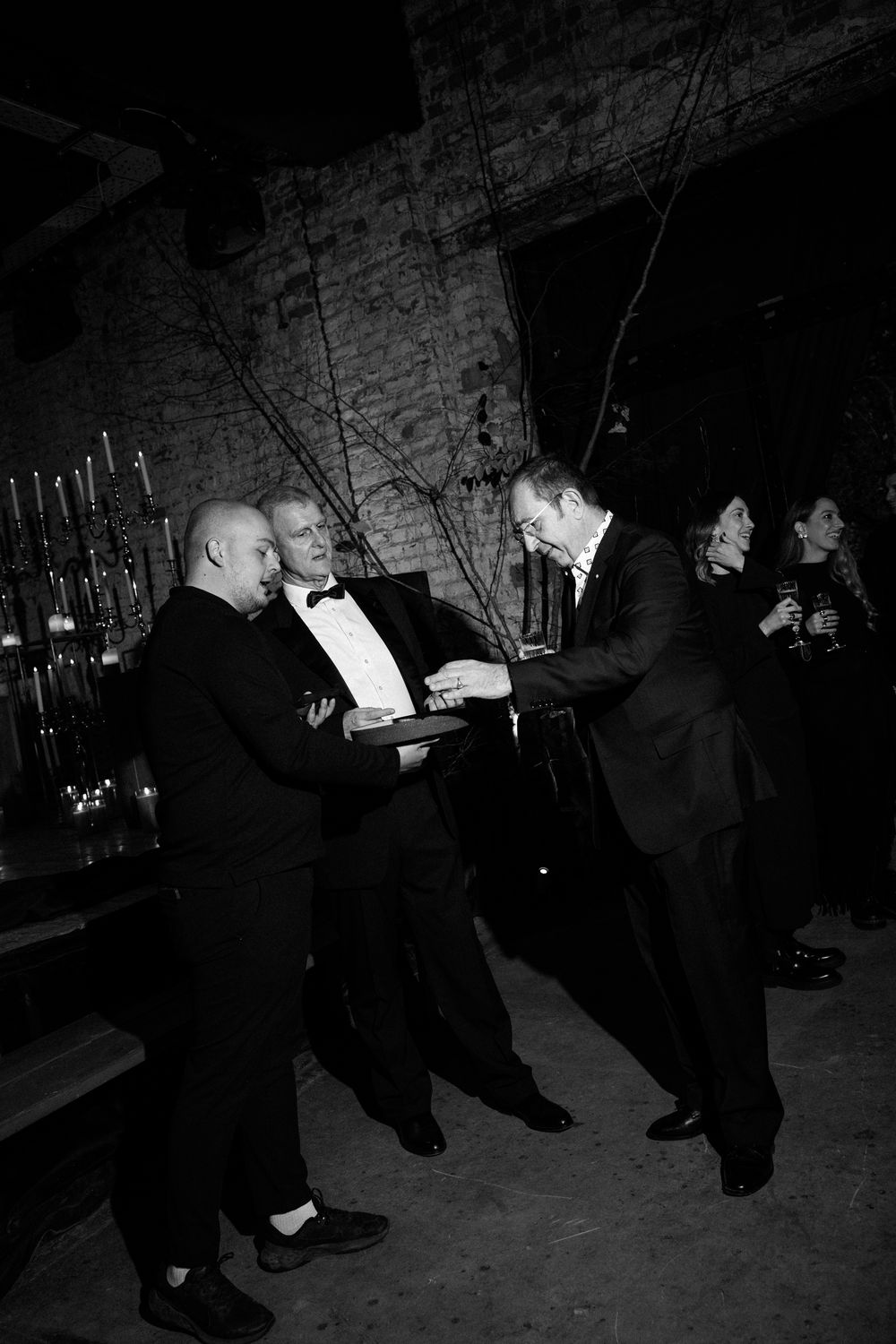 Men in formal attire interact at an elegant bar setting with candlelit ambiance. Block 33, Destination Wedding in Thessaloniki, Greece.