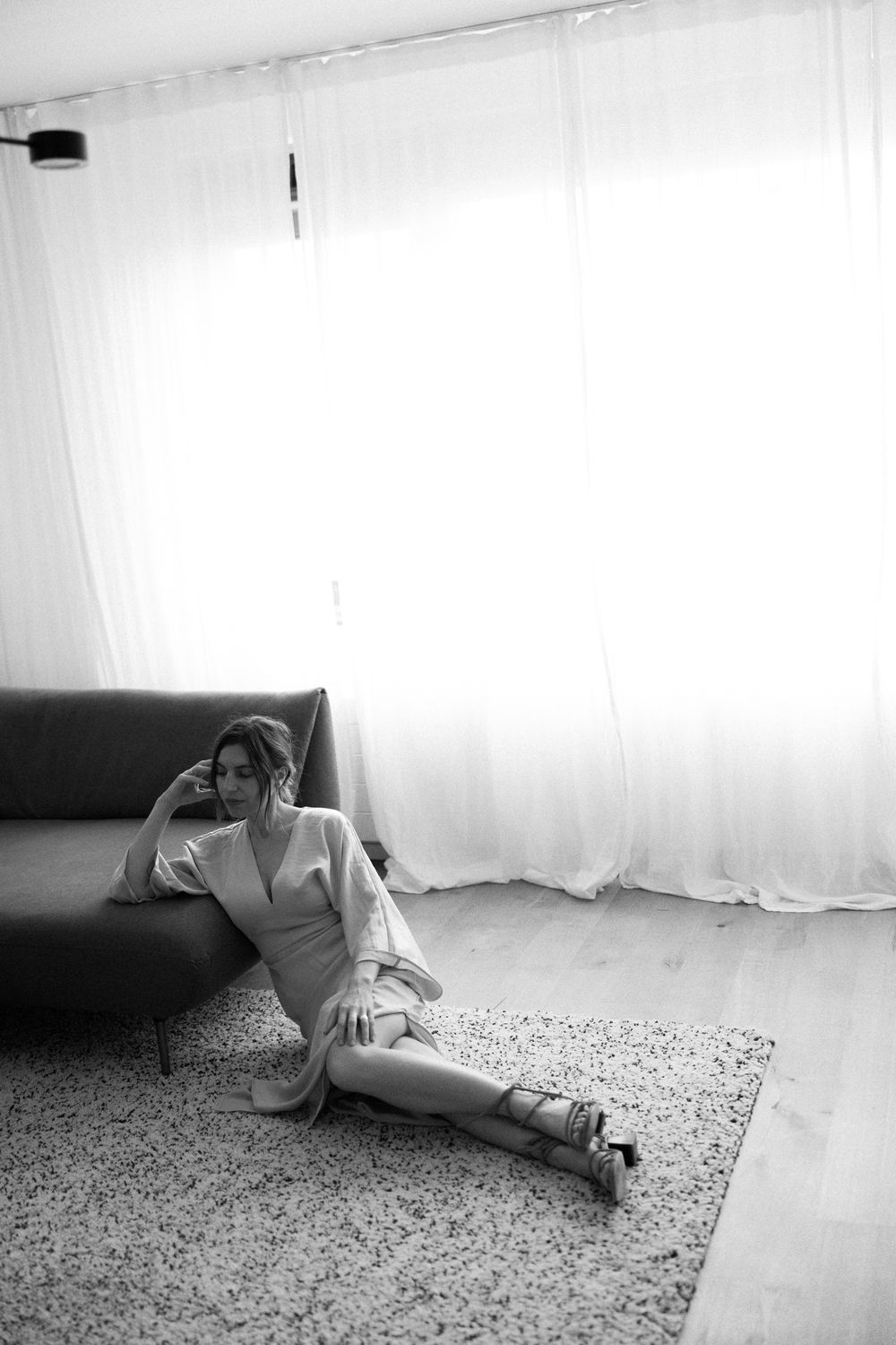 Artistic black and white photo of a bride reclining on dark couch near bright window. Rotterdam, The Netherlands.