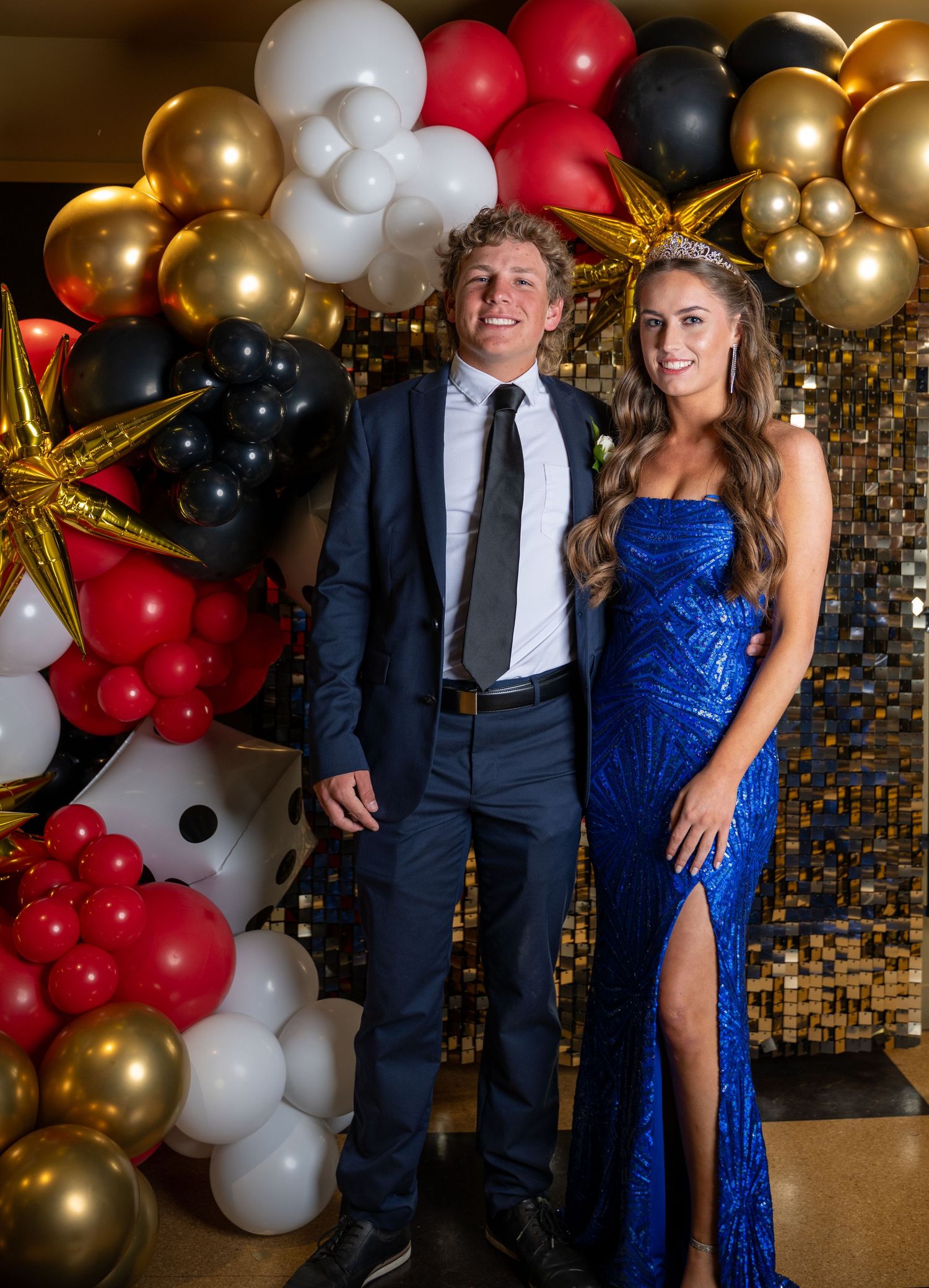 Couple posing in formal attire against balloon backdrop at special event.