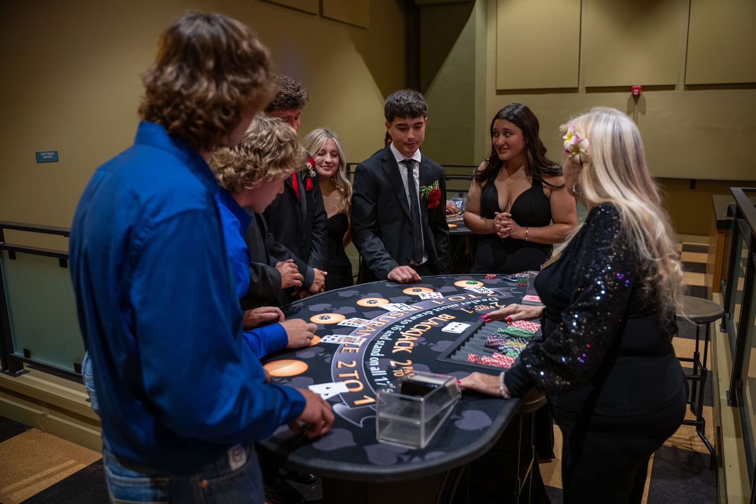 A group of people gather around a blackjack casino table as a dealer leads the game in an indoor venue.
