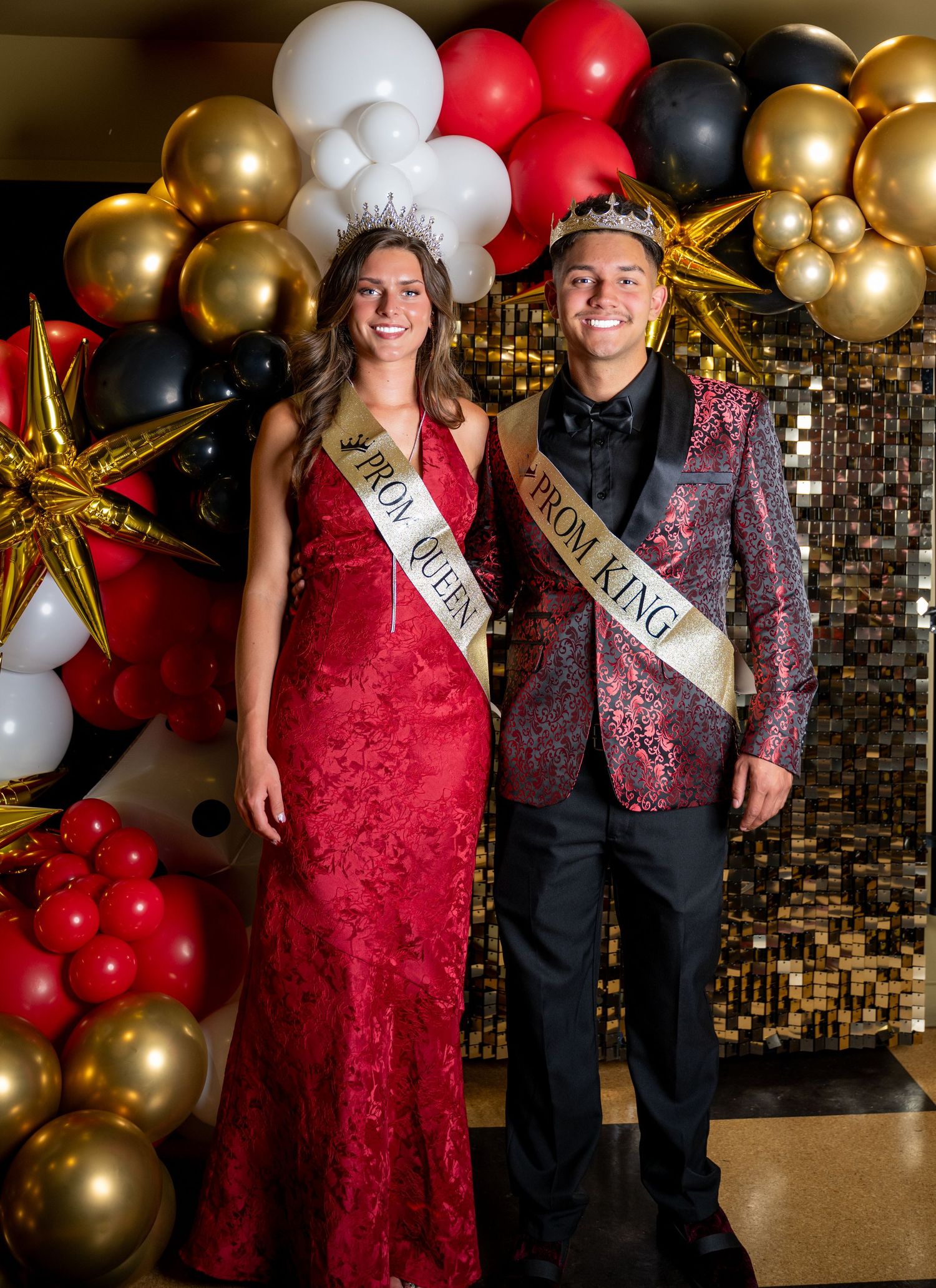 Prom royalty wearing formal attire pose in front of an elegant balloon display.