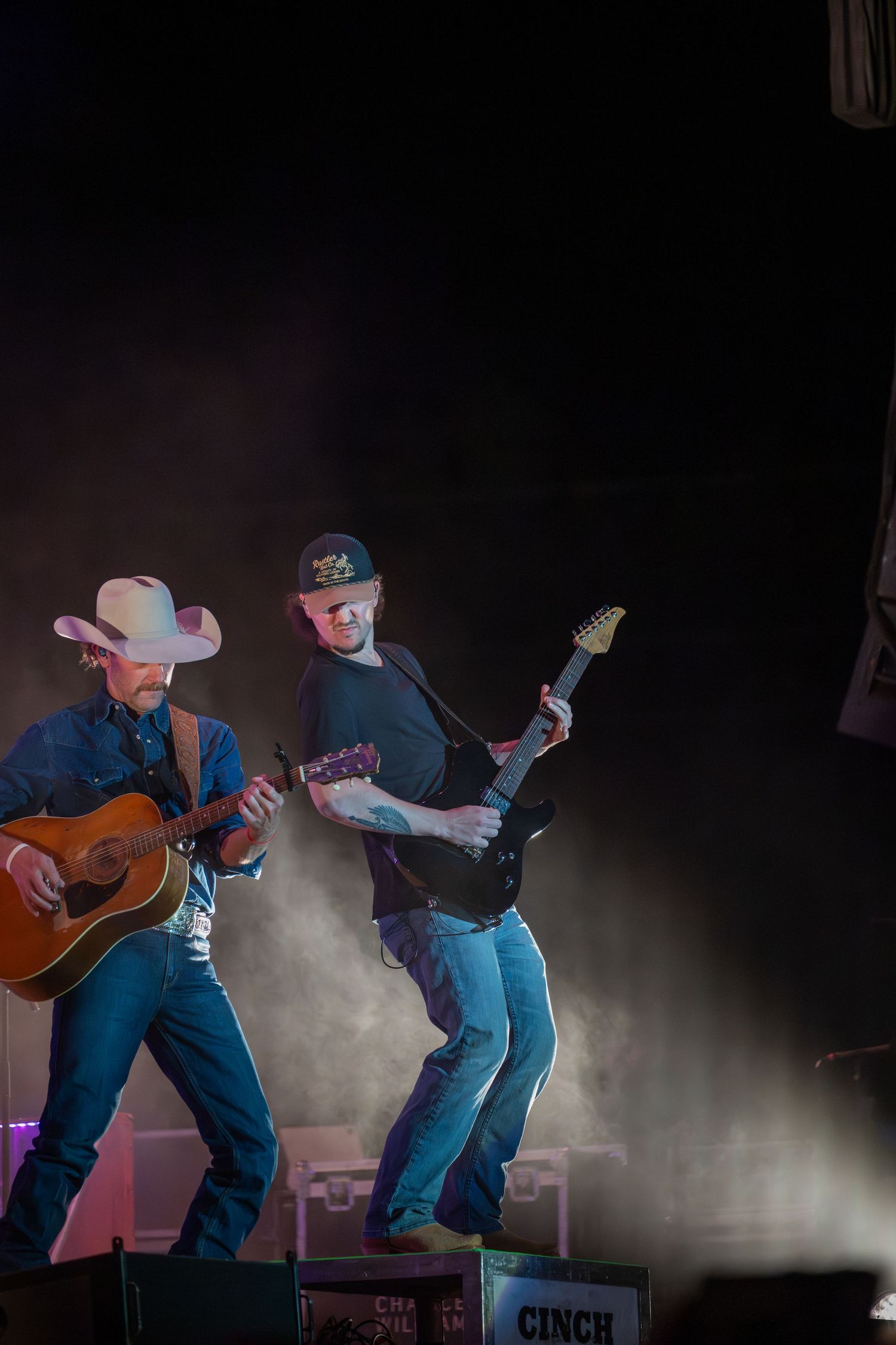 A sequence of performance shots shows a musician dancing while playing acoustic guitar on a smoky stage in blue jeans.