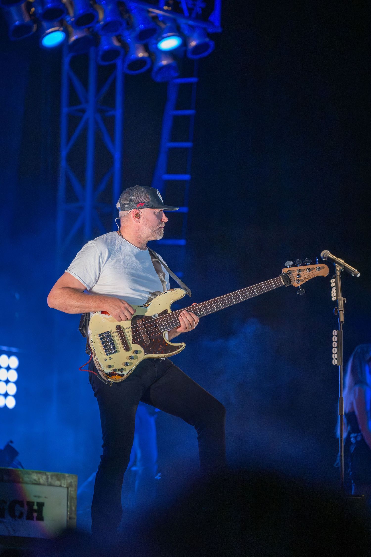 Musician performs on bass guitar against dramatic blue stage lighting during a live concert performance.