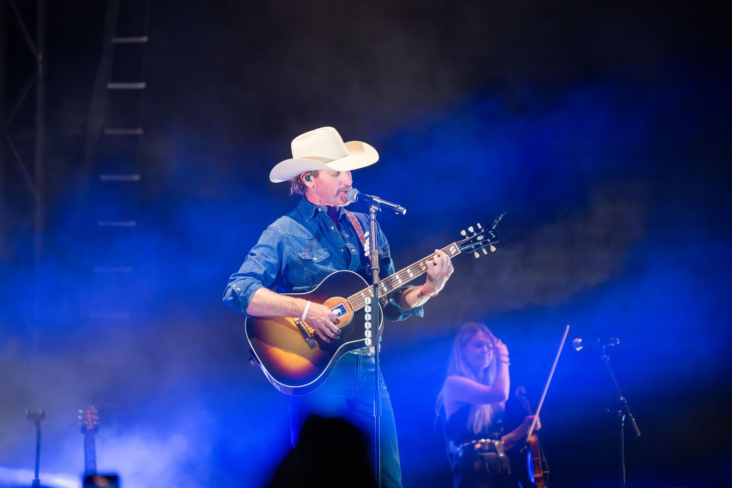 Country musician performs on stage with acoustic guitar under dramatic blue lighting during live concert performance.