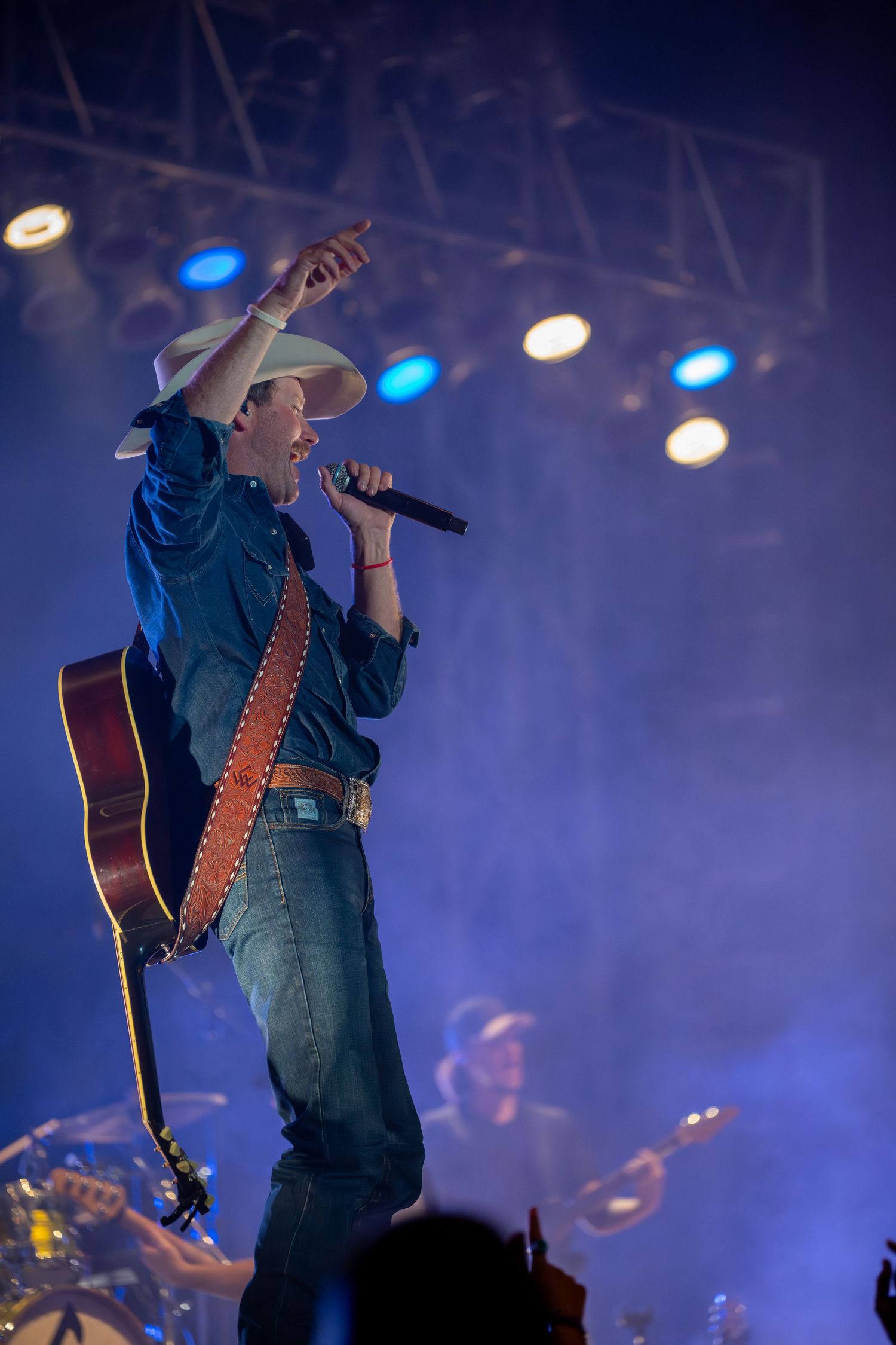 A performer in cowboy attire silhouetted against blue stage lighting while playing guitar during a concert performance.