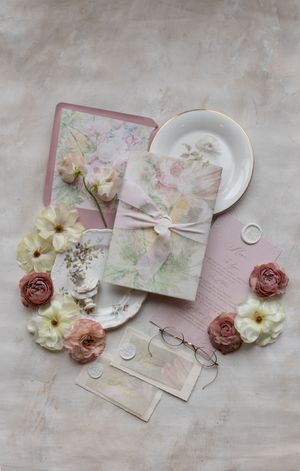 Feminine flat lay with vintage pastel flowers, delicate envelopes and plates with gold trim arranged on soft linen background.