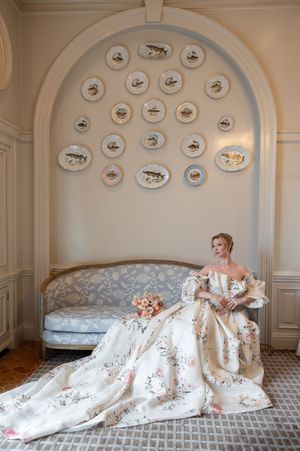 Elegant bridal portrait on antique settee beneath decorative plate wall display.