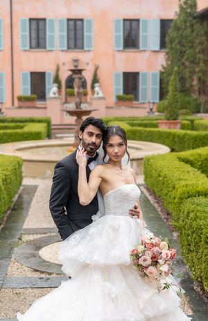 Romantic wedding portrait in front of Mediterranean-style villa with fountain and manicured gardens.