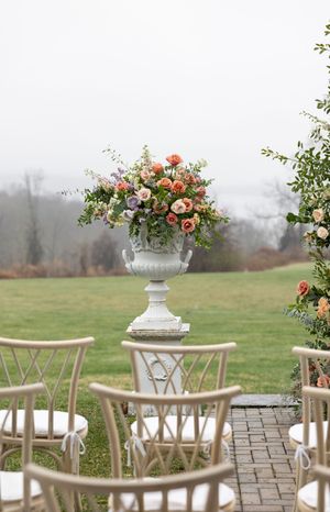 Romantic floral arrangement in white urn with misty outdoor ceremony setting.