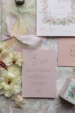 Soft pink wedding invitation suite with floral design and delicate ribbon on marble surface.