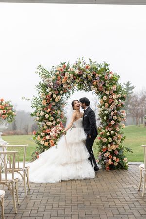 Newlyweds share a moment under a lush floral arch with pink and white roses.