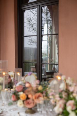 Elegant wedding reception table with floral centerpieces by a window with bare winter trees outside.