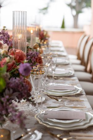 A close-up of a romantic tablescape with lilac flowers, crystal candle holders, and gold-rimmed place settings.