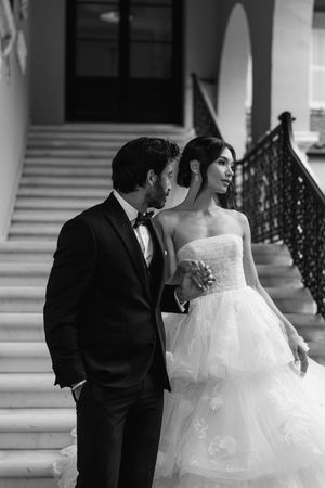 Black and white wedding photo of couple on grand staircase with ornate railing and elegant bridal gown.