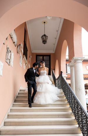 A romantic wedding moment on a grand staircase with peach walls, ornate railings and hanging vintage lantern.