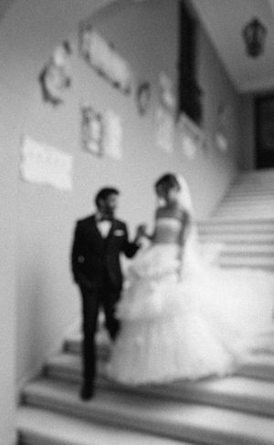 A blurry black and white photograph of a wedding couple ascending a staircase together in formal attire.