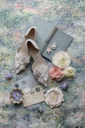 Wedding accessories including beige bow shoes, flowers, and vintage cards arranged on textured fabric.