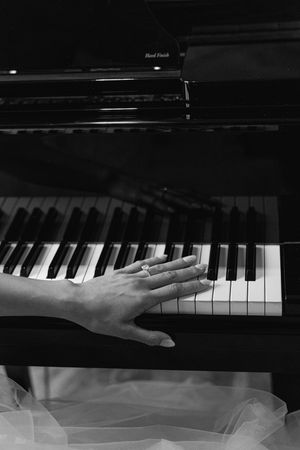 A person's hand resting gracefully on piano keys in dramatic black and white lighting.