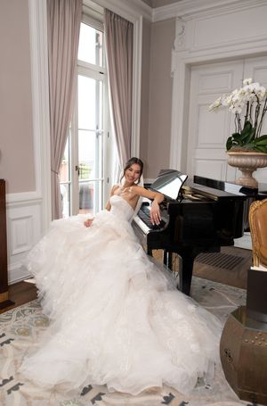 A stunning wedding dress with a flowing train elegantly draped over a grand piano in a luxurious room.