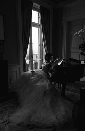 Silhouette of someone in a flowing gown playing piano by a sunlit window.