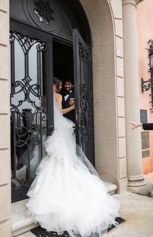 A stunning white wedding gown with flowing train showcased through ornate black iron doors at an elegant entrance.