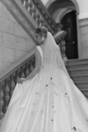 Black and white photo of a bride ascending stairs, showing the dramatic train of her wedding gown.