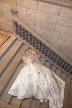 A stunning white wedding gown with a full skirt cascades down marble stairs beneath stone balustrades.