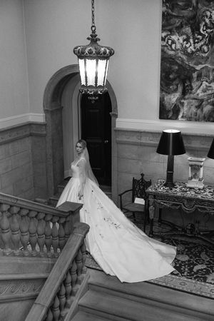 Elegant bride on grand staircase beneath vintage chandelier in black and white photography.