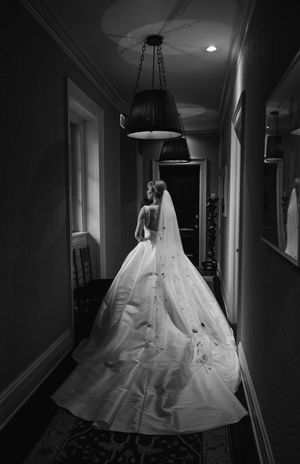 Dramatic black and white photo of a wedding dress with cathedral train in a dimly lit elegant hallway.