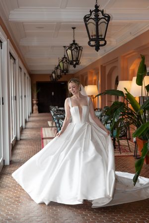 Bride twirling in elegant ballgown style dress in sunlit hallway with vintage lanterns.