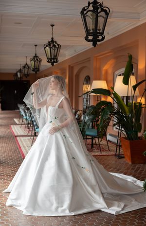 An elegant white wedding gown with long train and veil photographed in a vintage hallway with ornate lanterns.