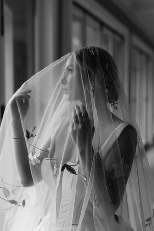 Ethereal black and white portrait of a bride underneath a delicate floral veil in soft window light.