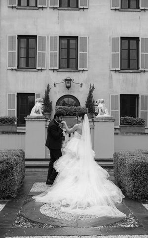 A black and white wedding portrait of a couple standing at an elegant building entrance.