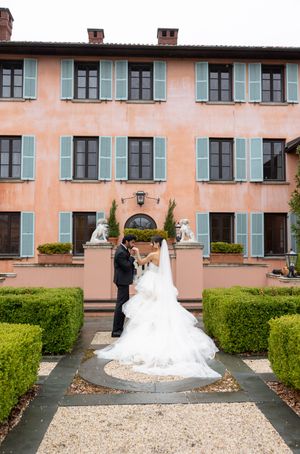 A view of a grand Italian villa facade with formal gardens and ornate architectural details in soft coral tones.