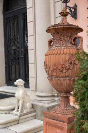 Decorative terracotta urn and stone dog statue flank elegant entrance doorway.