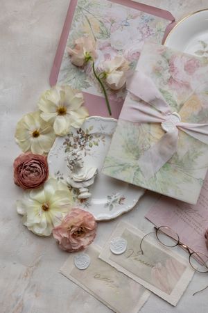 Romantic wedding stationery flatlay with pale flowers, wax seals and delicate pink details.