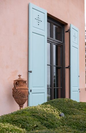 Light blue shuttered window with ornate terracotta urn on Mediterranean style building.