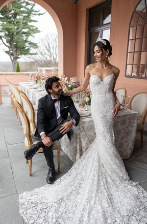 An elegant outdoor wedding scene with a couple on a terrace featuring coral walls and bistro chairs.