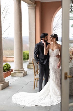 A romantic wedding couple sharing an intimate moment on an elegant veranda with stone columns.