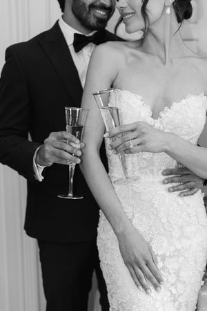 Elegant black and white wedding photo showing champagne toast with intricate lace dress details.