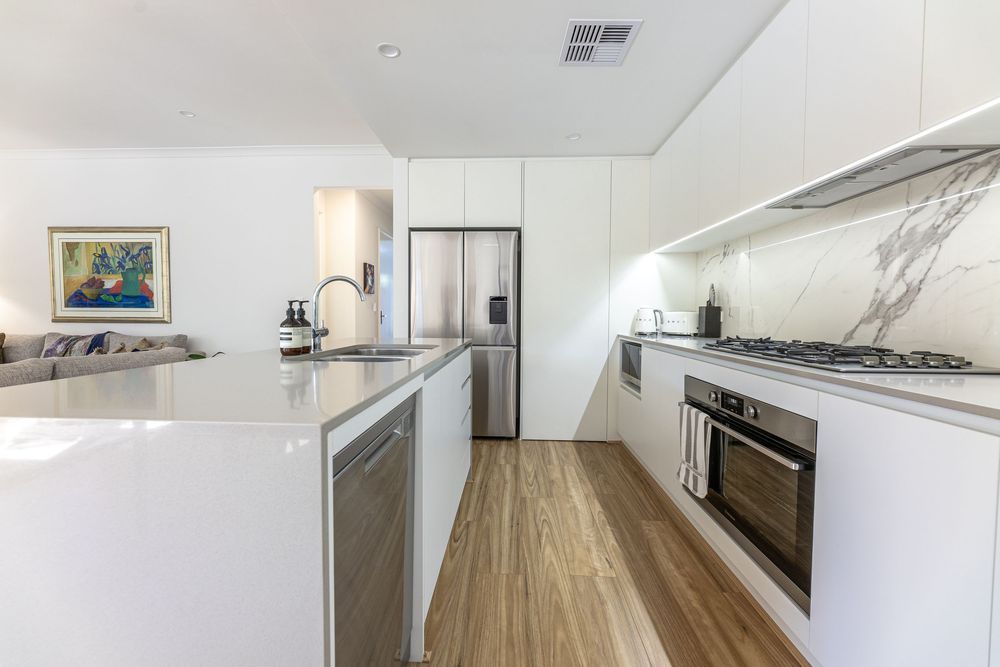 Modern white kitchen with marble design backsplash, stainless steel appliances, wood floors and beautiful countertops.