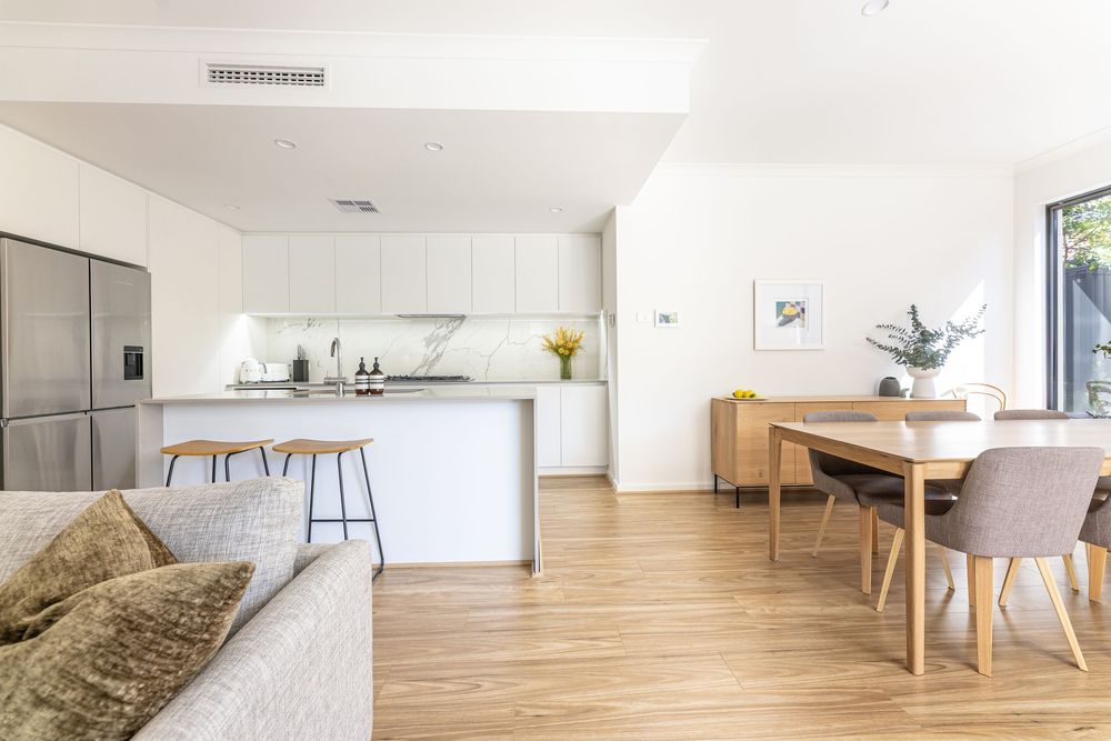 Modern open plan living space with white kitchen, wooden floors, dining area and plush brown throw on couch.