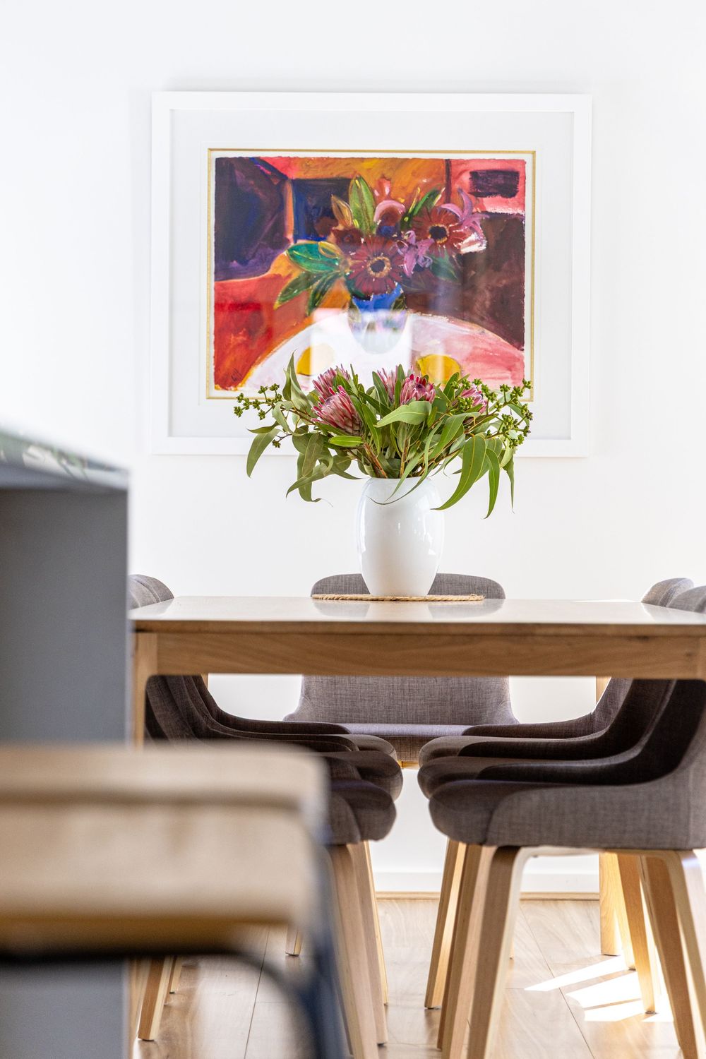 Modern dining room interior with white vase of fresh flowers on wooden table and colorful artwork on wall, Perth Real Estate Photography