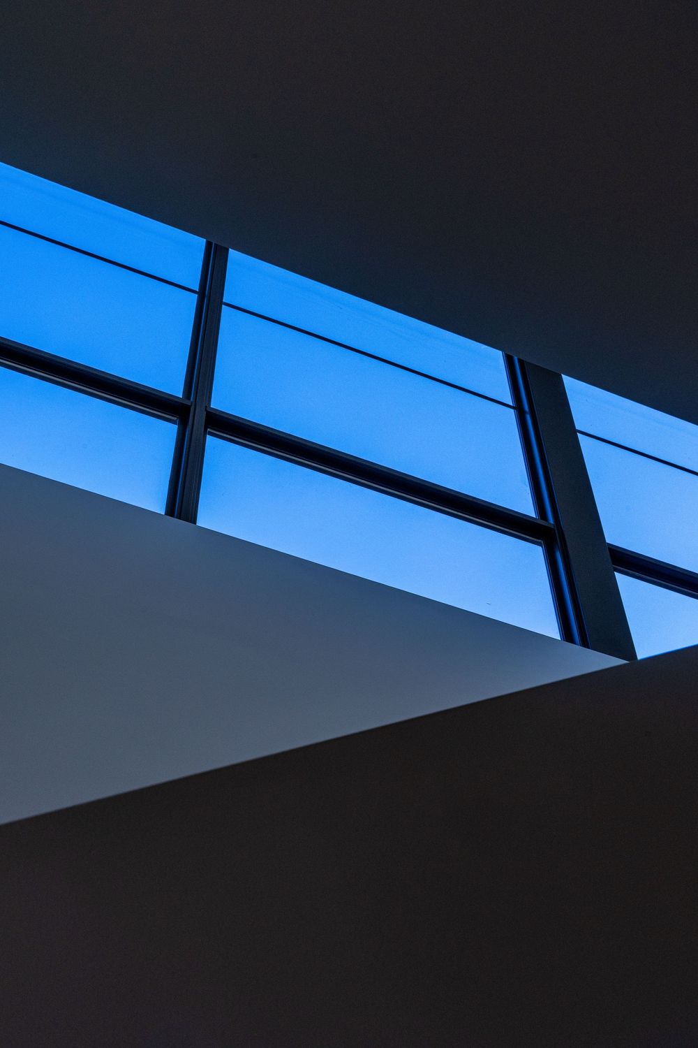 Minimalist architectural detail showing angled windows against a bright blue sky with stark geometric shadows by Kirsten Graham