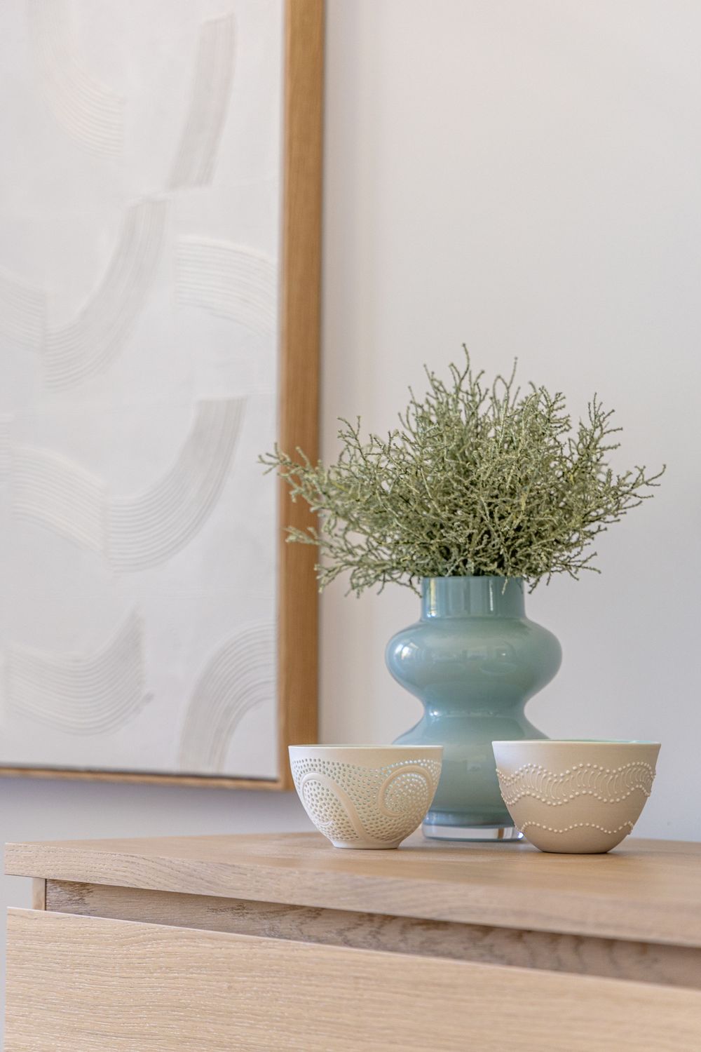 Elegant home decor featuring a blue ceramic vase with dried flowers and two textured ceramic bowls on a wooden cabinet.