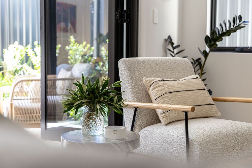 Cozy living room corner with boucle armchair, decorative pillows and potted plants by sunlit window. Commercial photo by Kirsten Graham